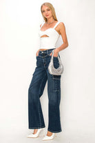 Woman wearing high rise wide jeans with a white top and holding a silver bag, showcasing a casual and modern style.