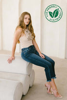 Woman wearing Corset High Rise Crop Flare Jeans with eco-friendly label, sitting on white furniture in a modern setting.