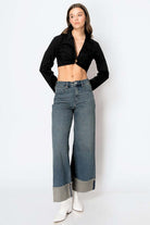 Woman wearing tummy control high rise cuffed wide leg jeans with a black crop top and white boots.