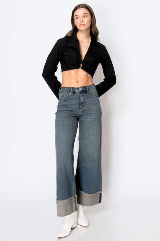 Woman wearing tummy control high rise cuffed wide leg jeans with a black crop top and white boots.