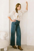 Woman wearing tummy control high-rise wide-leg jeans with cuff detailing, styled with a lace top and brown boots.